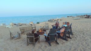 People sitting in chairs around a bonfire on the beach