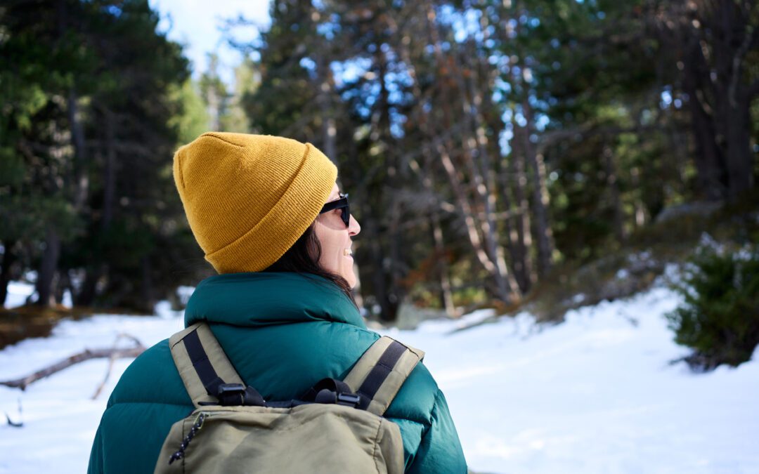 Rear View of Unrecognizable Woman Hiking in a Snowy Forest Wearing a Yellow Beanie and Backpack looking at view cheerfully. Copy space image.