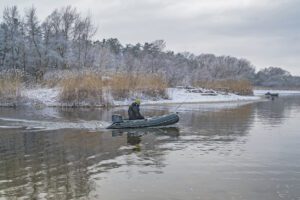 man in boat fishing on river in winter